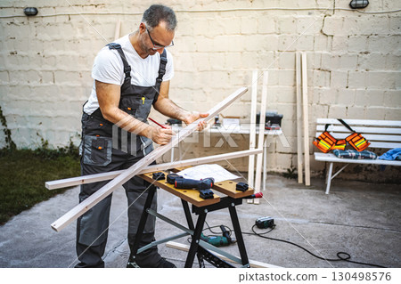 Mature male carpenter measuring wooden plank outdoors 130498576