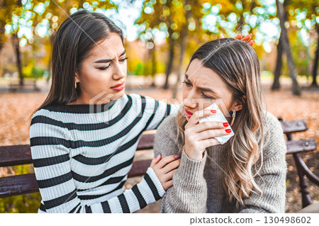 Two women are sitting on a bench and comforting each other 130498602