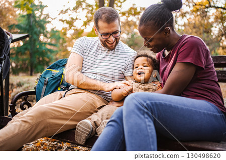 Mixed race couple is sitting on a park bench with their son Mixed race couple is sitting on a park bench with their son 130498620
