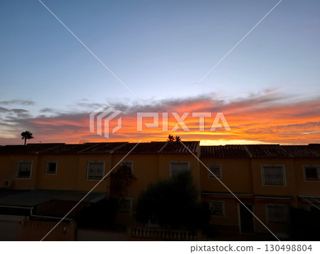 Brilliant orange hues fill the sky during sunset over quaint residences in Spain. The peaceful atmosphere reflects the charm of Mediterranean evenings, inviting tranquility and reflection. 130498804
