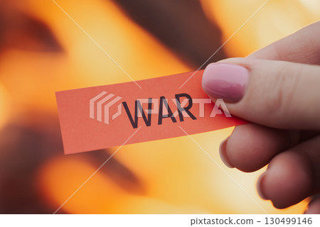 Red paper with inscription War in woman's hand near bonfire. Concept of destructive, bloody war, all the horror it bring to people 130499146