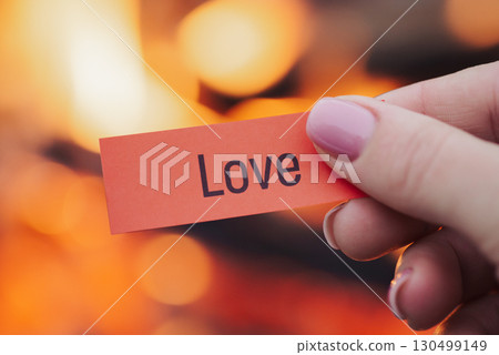 Paper with inscription Love in woman's hand with fire on the background. Hiding real feelings to somebody, don`t show your love, being afraid to get refusal 130499149