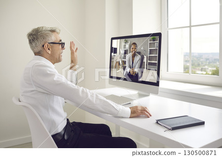 Man waving hello at the computer screen at the start of a virtual business meeting Man waving hello at the computer screen at the start of a virtual business meeting 130500871