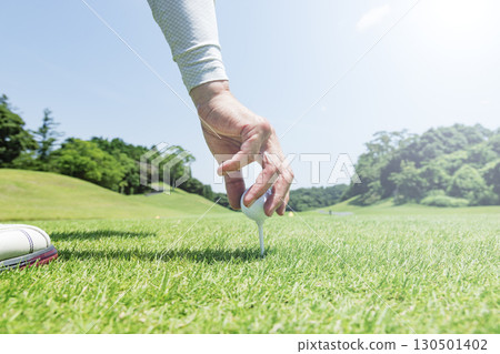 雙手將高爾夫球放在綠樹成蔭的發球區上的發球座上 雙手將高爾夫球放在綠樹成蔭的發球區上的發球座上 130501402