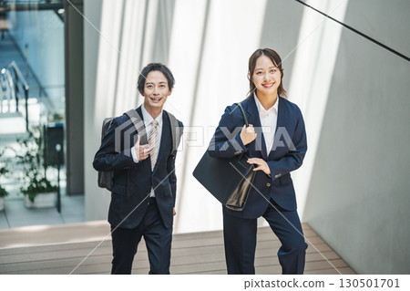 穿著西裝的年輕男女走上辦公大樓的樓梯 穿著西裝的年輕男女走上辦公大樓的樓梯 130501701