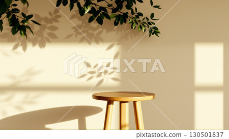 A simple wooden table with a round top filled with a coating that provides sunlight. The delicate shadows of leafy branches play on the textured cream wall in the background. 130501837