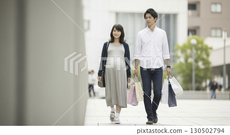 一位孕婦和她的丈夫剛買完孕婦用品回家，丈夫扛著所有的行李。 130502794