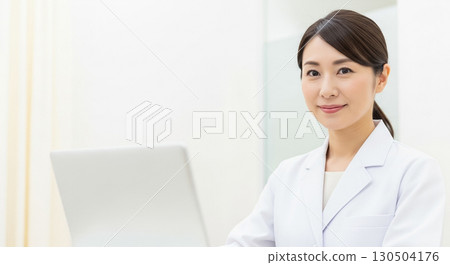 A young woman wearing a white coat in front of a laptop 130504176