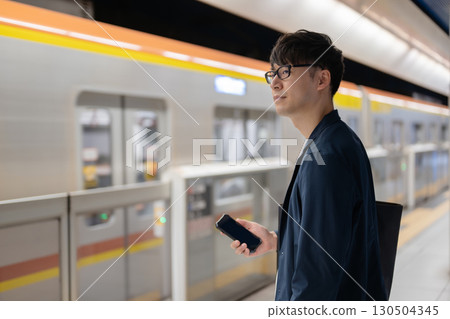 A man waiting for a train on the station platform 130504345
