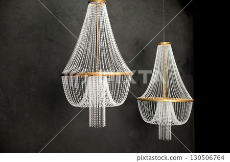 Elegant crystal chandeliers hanging against dark textured background in luxurious setting Elegant crystal chandeliers hanging against dark textured background in luxurious setting 130506764