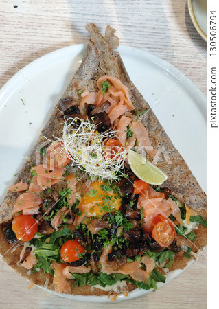 Savory buckwheat crepe with smoked salmon, cherry tomatoes, and fresh herbs on white plate 130506794