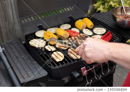 Grilling vegetables and corn on barbecue grill with male hand tongs 130506804