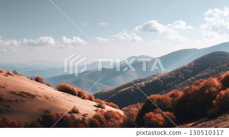 Golden autumn hills cascade down to vibrant orange trees with misty blue mountains rising under the sky 130510317