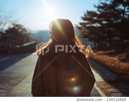 A Korean woman stands on a path her hair beautifully backlit by the brilliant sun 130510408