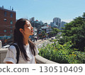 A serene Korean woman looks up illuminated by the sun taking in the city view 130510409