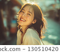 A beautiful Korean woman smiles with pure joy her dark hair glowing in the golden sunlight 130510420