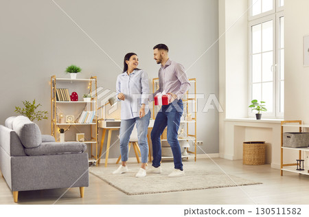 Young happy man and woman standing with present gift box in the living room at home. 130511582