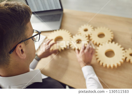Smart young man connecting cogwheels on his office desk as a symbol of business integration Smart young man connecting cogwheels on his office desk as a symbol of business integration 130511583