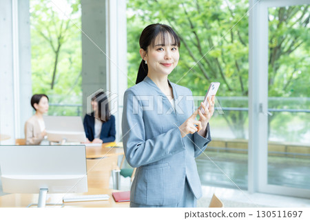 經營一部智能手機的女商人在辦公室 130511697