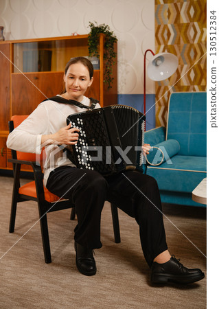 A middle-aged woman playing the accordion while seated in a cozy living room during the afternoon 130512384