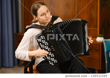 A middle-aged woman plays an accordion while seated indoors, showcasing her musical talent during a cozy evening A middle-aged woman plays an accordion while seated indoors, showcasing her musical talent during a cozy evening 130512385