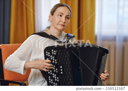 A middle-aged woman playing the accordion indoors during a music session in a cozy setting A middle-aged woman playing the accordion indoors during a music session in a cozy setting 130512387