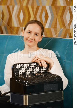 Middle-aged woman enjoying music while sitting with an accordion in a vibrant indoor setting 130512388