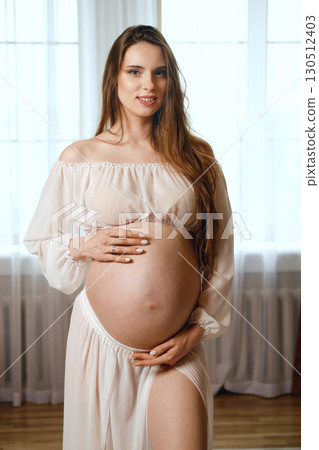 Expecting mother celebrates pregnancy in elegant attire at home during bright afternoon 130512403