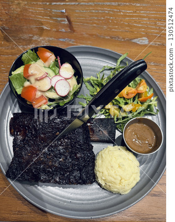 Gourmet plate with grilled beef short rib, mashed potatoes, salad with dressing, fresh greens and tomatoes, fine dining restaurant food presentation 130512474