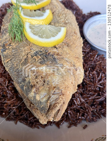 Whole fried fish topped with fresh lemon slices and dill, served over spiced rice with creamy sauce, gourmet seafood dish for festive dining and culinary presentation 130512478