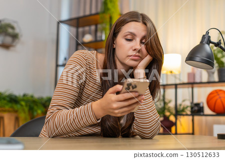 Young woman bored scrolls news on smartphone unhappy tired from very repetitive social media updates 130512633