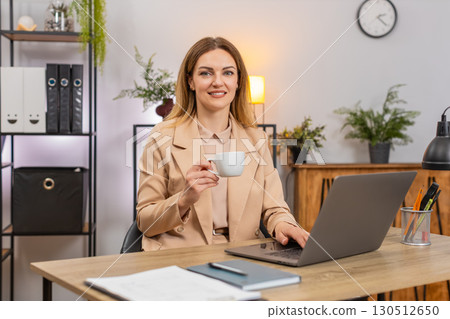 Businesswoman enjoys coffee while working on laptop takes sip smiles refuels energy keeps going 130512650