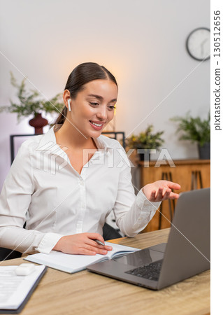 Young businesswoman on laptop video call greets nods takes notes and sets clear deadlines with team Young businesswoman on laptop video call greets nods takes notes and sets clear deadlines with team 130512656