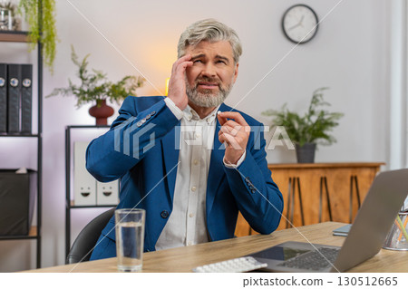 Middle-aged businessman massages temples swallows headache pill drinks water again to return to work 130512665