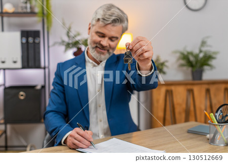 Middle-aged happy businessman signs lease holds apartment keys smiles celebrating lease approval 130512669