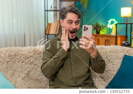 Middle-aged man shocked reading wow news on smartphone eyes wide cheering joyful surprise great win Middle-aged man shocked reading wow news on smartphone eyes wide cheering joyful surprise great win 130512735