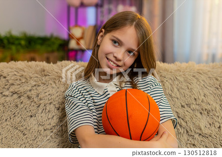 Child girl kid playing alone on sofa at home tossing basketball ball in air enjoying solo indoor fun 130512818
