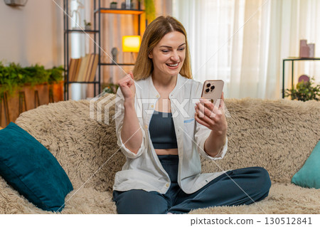 Adult happy woman celebrating lottery win on smartphone smiling with joy and making victory gesture 130512841