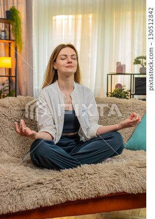 Woman meditating peacefully on home sofa, calm expression, eyes closed, relaxation, taking a break 130512842