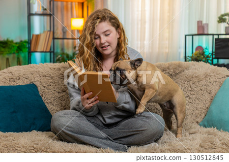 Young woman reading bedtime story to pug dog on home sofa, peaceful end of day with emotional care Young woman reading bedtime story to pug dog on home sofa, peaceful end of day with emotional care 130512845