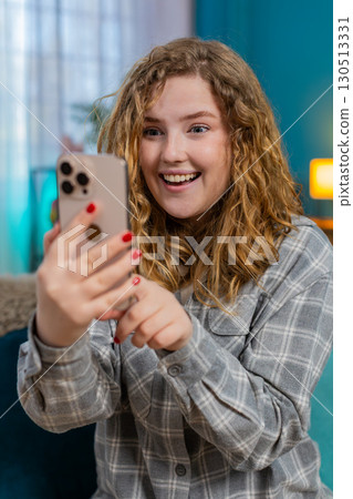 Young woman sitting on sofa smiling with joy reacting to long awaited message on smartphone happily Young woman sitting on sofa smiling with joy reacting to long awaited message on smartphone happily 130513331