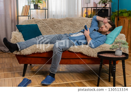 Young man unexpectedly falling asleep on sofa while holding smartphone in hand, tired and exhausted 130513334