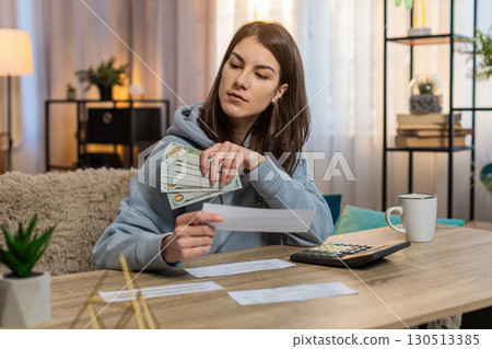 Young woman counting money while sitting on sofa with receipts and calculator on tablet at home Young woman counting money while sitting on sofa with receipts and calculator on tablet at home 130513385