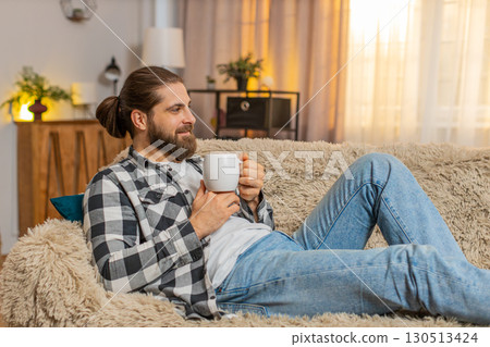 Young man lying with coffee mug at home, sofa calm, quiet break, easy smile, stress-free peace vibe Young man lying with coffee mug at home, sofa calm, quiet break, easy smile, stress-free peace vibe 130513424