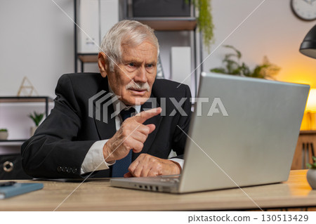 Angry senior freelancer businessman in suit making webcam laptop online video call at home office Angry senior freelancer businessman in suit making webcam laptop online video call at home office 130513429