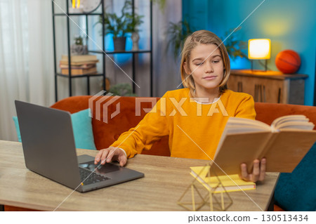 Teenager boy doing online homework on laptop, reading book and taking notes on couch at home room Teenager boy doing online homework on laptop, reading book and taking notes on couch at home room 130513434