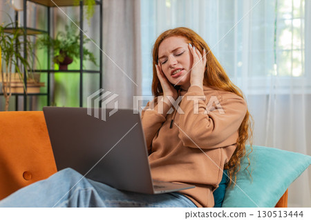 Tired young woman using laptop suffering from headache problem tension and migraine stress at home 130513444