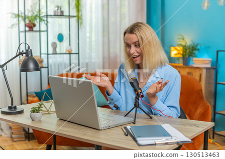 Happy blogger woman recording podcast at desk, giving workshop webinar speaking at microphone laptop 130513463