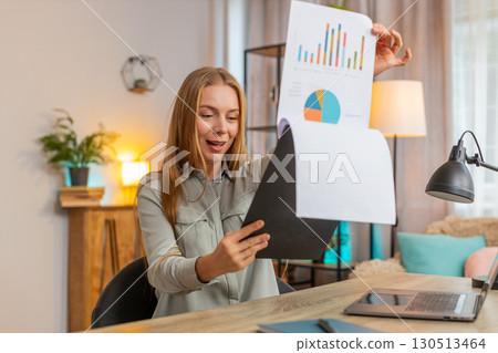 Happy mature businesswoman freelancer analyzing graph documents sitting at home office table desk 130513464