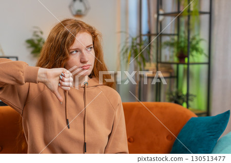 Upset woman showing thumb down sign gesture, expressing discontent sitting on sofa couch at home 130513477